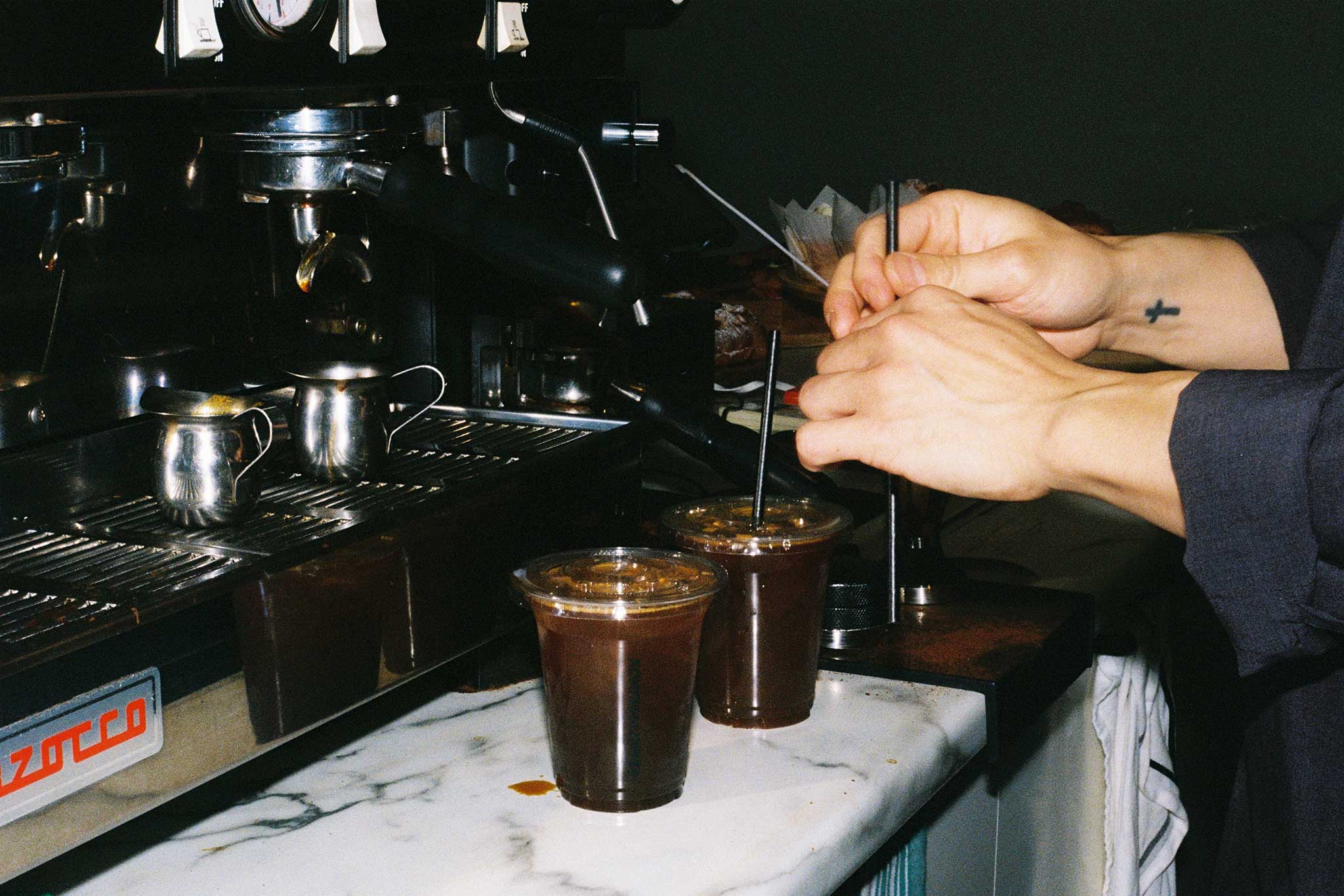 Iced coffees photographed on 35mm film. Barista behind the bar making iced coffee. 35mm aesthetic brand social media imagery for cafés and bars.