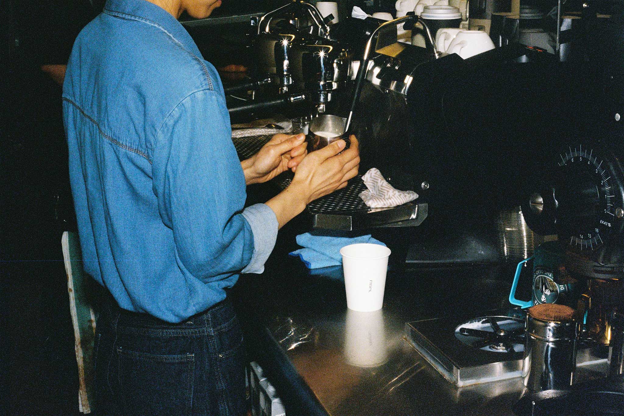 Barista steaming oat milk for coffee at specialty coffee shop, Rumours. Café brand photography ideas, 35mm film with direct flash.